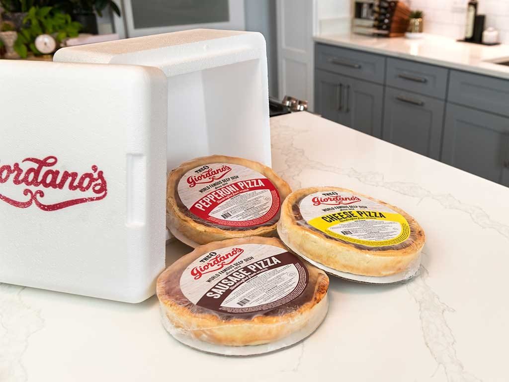 Giordano's shipping cooler with packaged pizzas on a kitchen counter