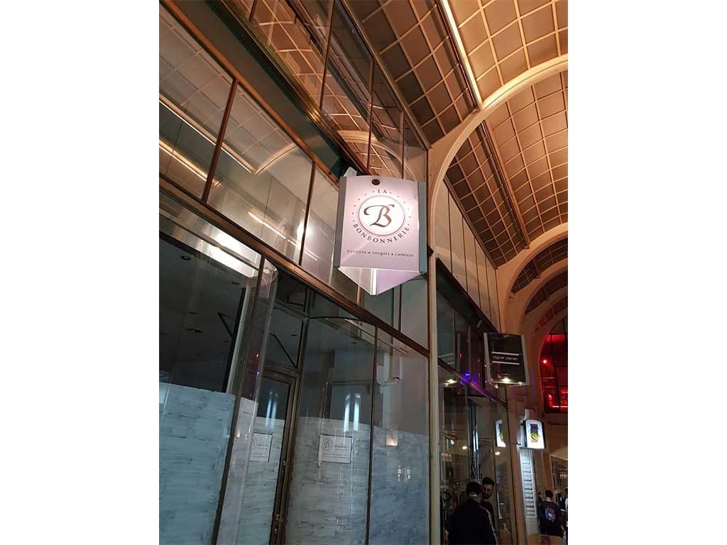La Bonbonnerie hanging blade sign in a glass-roofed gallery