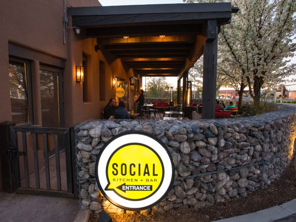 Lit Social Kitchen and Bar entrance sign on a stone patio wall
